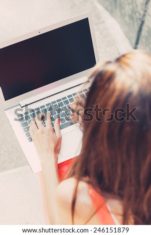 Girl using laptop sitting on the stairs outdoors. Back view. Dark screen