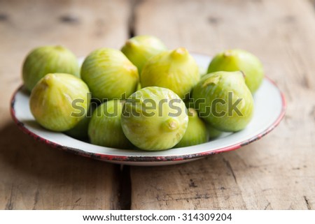 Old dish full of green ripe figs on a rustic wooden table