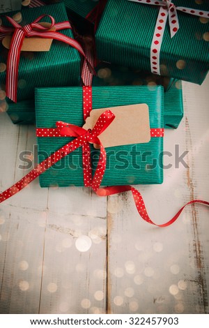 Christmas packages with green paper, red bow and brown label on a white wooden table. Lights effect added