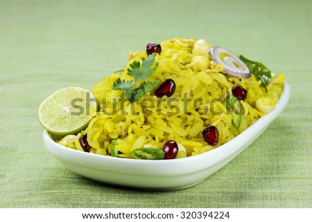 Indian breakfast Poha topped with peanuts, pomegranate seeds, chopped green chilly, onion, lime, coriander leaves and curry leaves.