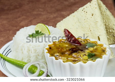 Cooked rice and cooked Arhar or Toor dal (Pigeon Pea) served with roasted papad, sliced onion and green chilly an Indian platter.