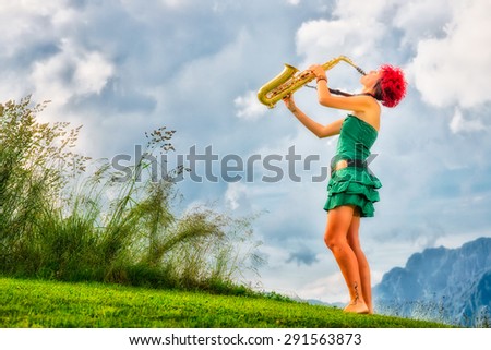 Young saxophonist (woman with the red hair) playing saxophone in the mountain nature.