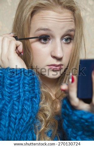 Young beautiful woman doing her makeup with a small mirror