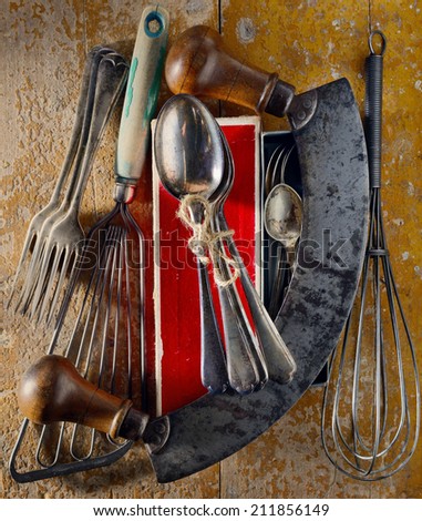 Collection of vintage kitchen utensils and silver spoons found at a flea market arranged on a grunge wooden surface. Directional light.