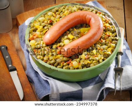 Smoked sausage on mushy peas, ham and onion dish. Traditional Dutch winter food in rustic setting.