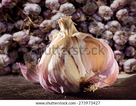 Garlic bulb on rustic wooden surface with stacked garlic bulbs as background. Selective focus close up on garlic bulb.