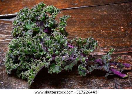 Kale leaves close up on rustic wooden surface. Red or Russian kale showing purple veins contrasting with green leaf.