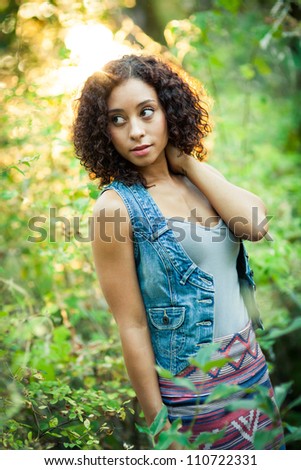 A young black woman gazes into the distance in a forest.