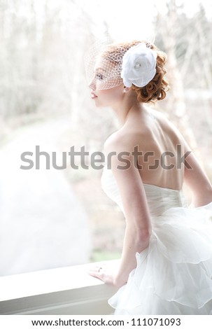 Red haired bride leans against porch railing, looking contemplative.