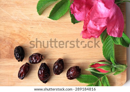 dried rose hip fruit and fresh rose flowers wooden kitchen board