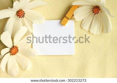 empty blank piece of paper with yellow clothes pin fresh flowers fabric background warm vintage golden tones