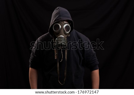 Man in black clothes wearing a classic gas mask over a dark background