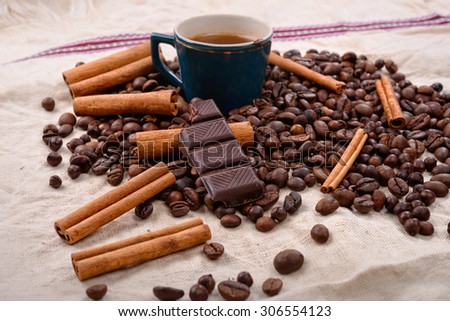 Cup of hot coffee with cinnamon sticks, bitten bar of chocolate on vintage texture background, selective focus