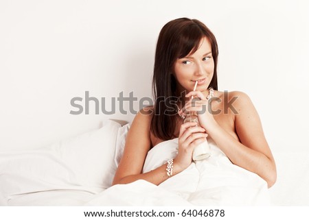 Young beautiful woman drinking milk sitting on white bed