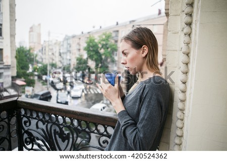 https://image.shutterstock.com/display_pic_with_logo/1085930/420524362/stock-photo-beautiful-young-girl-with-a-cup-of-morning-coffee-standing-on-the-balcony-in-the-rain-thinking-420524362.jpg