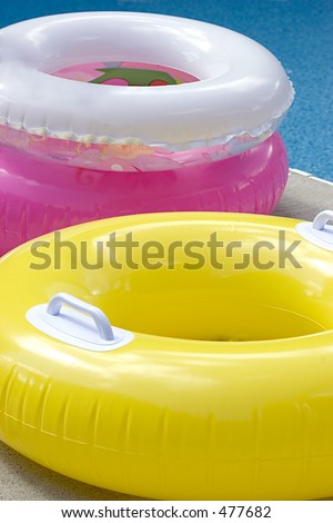 Three swimming pool inner tubes in yellow, pink and white.