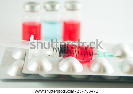 Red liquid in disposable syringe on blister pack on medicine vials background