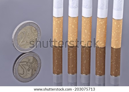 Cigarette and the 2 Euro coin on a reflective surface . Smoking is a waste of money