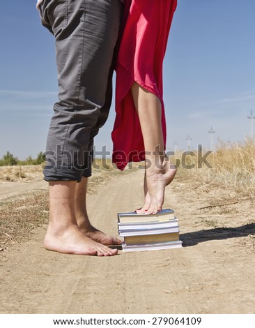 A girl stands on a stack of books to reach out and kiss the guy