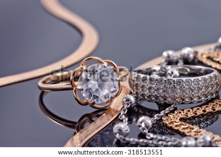 Gold, silver rings and chains of different styles are lying together on the reflecting surface