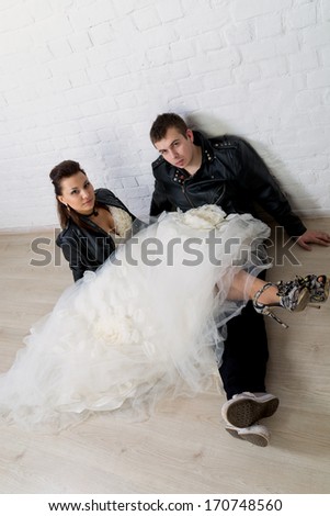 young stylish couple in black leather clothing sit on the floor near the wall