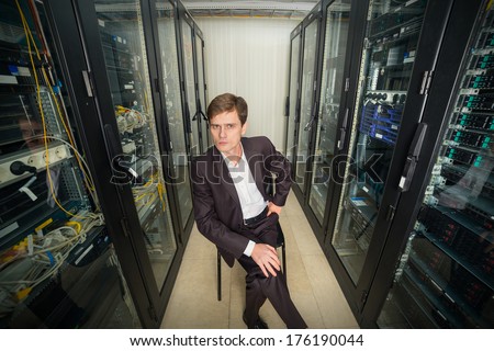 Network Engineer in the server room in a suit sitting on a chair, distorted perspective