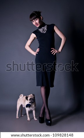 Beautiful fashion brunette girl in a dress together with a pug dog in a bow tie in a studio environment