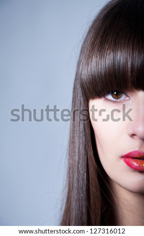 Studio portrait of pretty young female model with straight hair, long straight fringe, natural makeup and bright colorful red glossy lips, looking at camera. Half face. Gray background, copy space