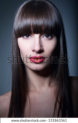 Young pretty woman model with healthy long straight hair, fridge, clear skin, elegant glamour makeup with slightly open glossy colorful red orange lips, looking at camera. Gray background