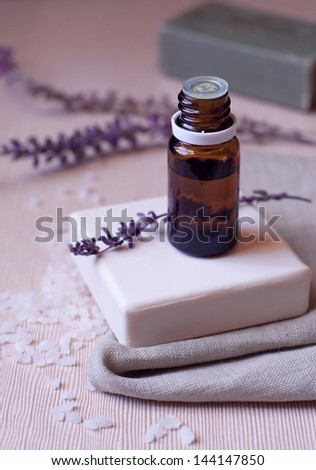 Spa products natural white and green bars of soap on olive oil, aroma oil bottle for aroma therapy, dry flowers of lavender on top of soap and at background, sea salt on the wooden table surface