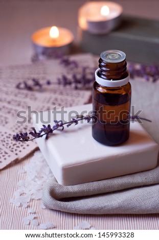 Spa products natural white bar of soap on olive oil, aroma oil bottle for aroma therapy, dry flowers of lavender on top of soap and at background, sea salt, burning candles on the wooden table surface