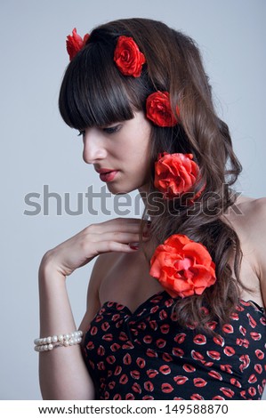 Pretty young woman model with red lips, elegant long brunette hair weaved into wave with big fresh terracotta roses, white pearl bracelet on hand, black corset with red lips pattern. Looking at camera