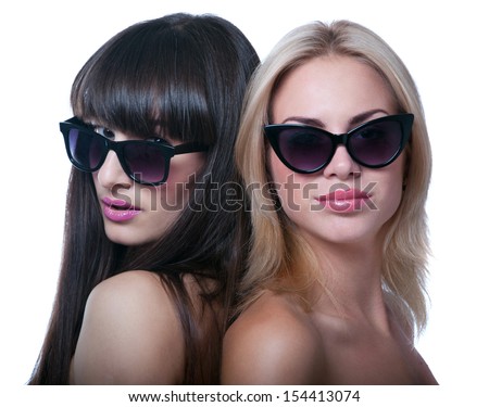 Studio portrait of two young beautiful women models wearing bright pink lipstick, sun glasses, smiling and looking at camera. Isolated on white background