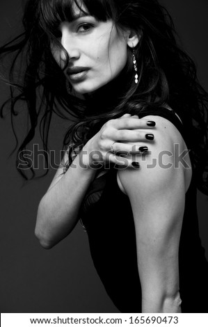 Black white studio portrait of young sexy brunette woman model wearing tight black dress, stripped bra, dark lipstick, black nail polish, looking at camera, wind blowing, disheveling long curly hair