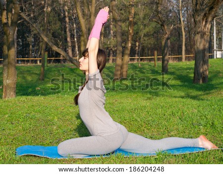 Beautiful woman practicing yoga outdoors on a warm spring day in a park, sitting, doing an asana on a yoga mat on the grass