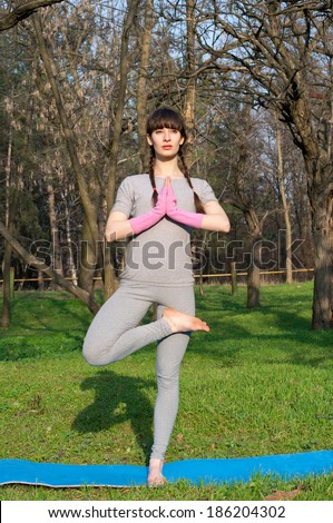 Beautiful woman practicing yoga asanas outdoors on a warm spring day in a park, keeping balance while doing a tree pose