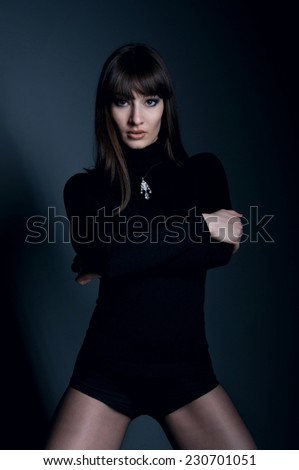 Studio portrait of beautiful woman model with straight long hair, wearing black clothes, black manicure, tights, pendant on her neck. Gray background
