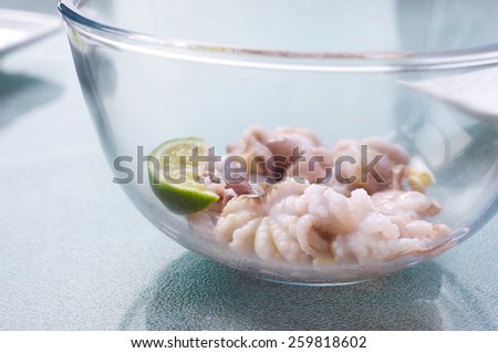 Fresh baby octopus being pickled with lime slice, garlic and olive oil in a glass bowl before cooking. On the table, still life, copy space