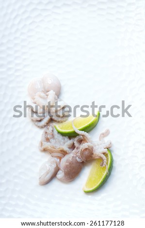 Still life of fresh baby octopus being pickled with lime slices on a white plate. On the plate, still life, copy space