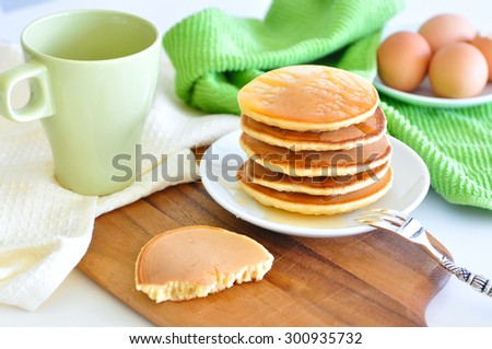 Delicious golden pancakes cooked on dry pan and served for breakfast with honey and kiwi fruit on a wooden board, one pancake half eaten. Still life, copy space