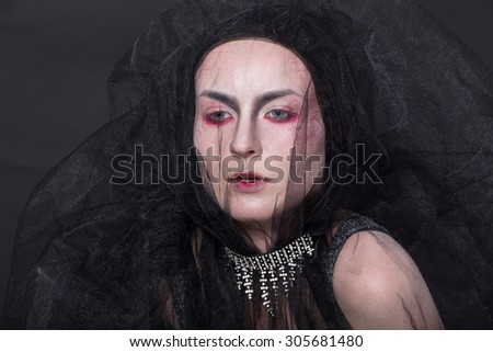 Art picture of a girl with stylish make-up in shades of red , covered with fabric - tulle on a black background