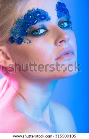Studio beauty girls photo blonde girl with creative make-up with stones with colored lights on a light background