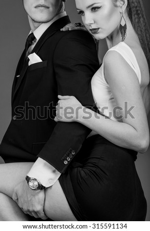 black and white Studio photos erotic young couple on black background. Girl in a dress, man in a business suit