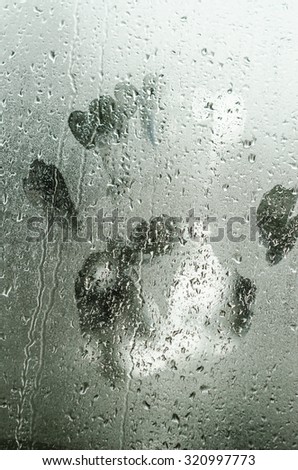 Water drops on glass window with a human hand shape imprinted