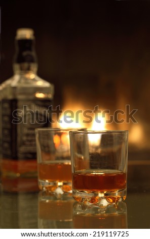 Two glasses  of whiskey and whiskey bottle on the background near the fireplace