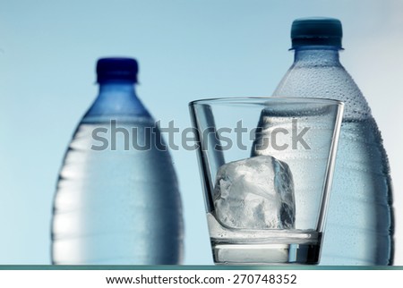 Water glass with ice cubes and mineral water bottles
