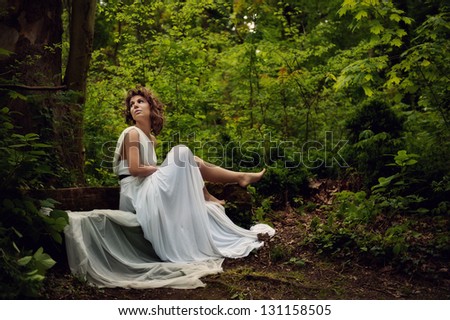 Young fairytale woman sitting on a bank in the woods, searching for something