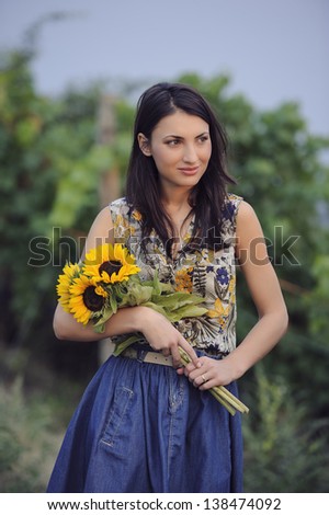 Beautiful delicate girl on a photo session in a vineyard, holding a sunflower bouquet