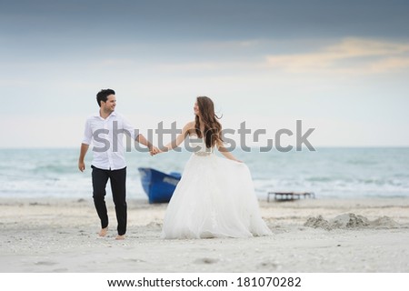Bride and groom running at a photo session, near a boat close to the sea