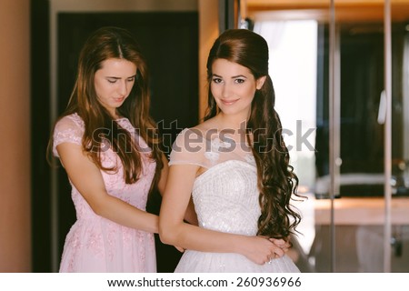 Beautiful bride getting dressed by her best friend in her wedding day
